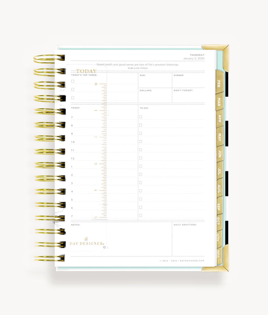 A small gold-colored bookmark ruler with weekend days marked, attached to a bright gold-binding daily planner.