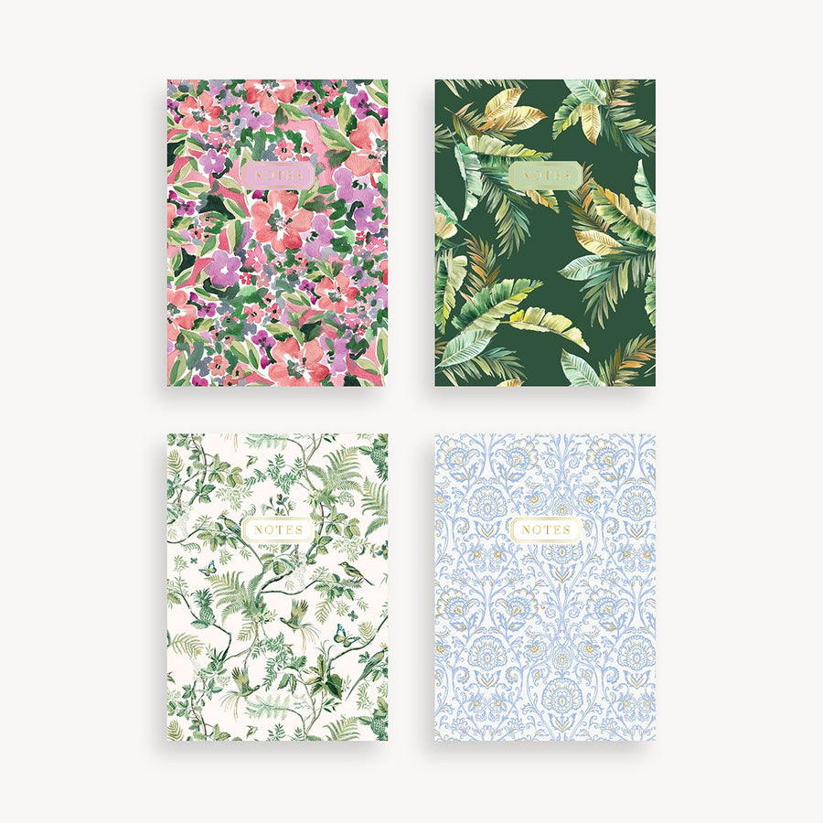 set of four slim mini notebooks with four red, pink, purple floral, green palm, green floral, and blue and gold repeated design in different cover patterns and gold title accent