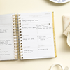 mini weekly planner, open book, written on pages, gold binding and tabs, beige background, dish, cup, cloth