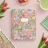 Notebook with colorful floral and building design on a pink surface with tulips and a map.